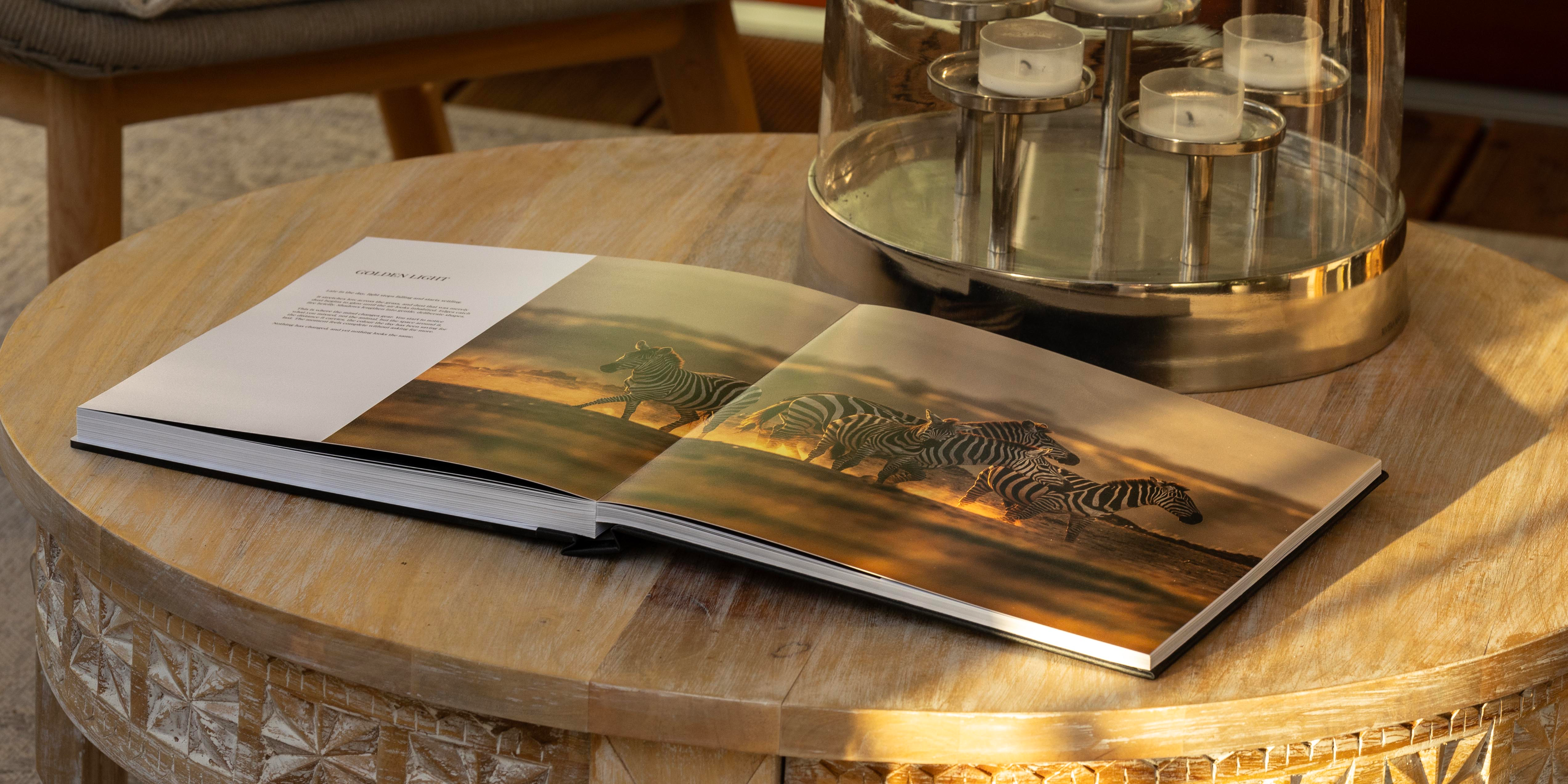 The Solio book lying open on a round wooden table in late afternoon light, showing the Golden Light spread of zebras